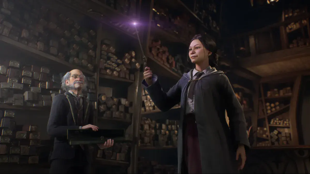 Une élève de Poudlard lève sa baguette lumineuse devant Ollivander dans sa boutique, dans le jeu Hogwarts Legacy de Warner Bros. Games